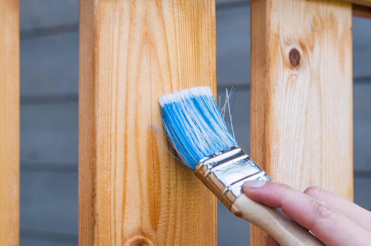 The Art of Drawing Readers In: Your attractive post title goes here A hand painting a wooden fence plank with a blue paintbrush outdoors. Perfect for DIY and renovation themes.